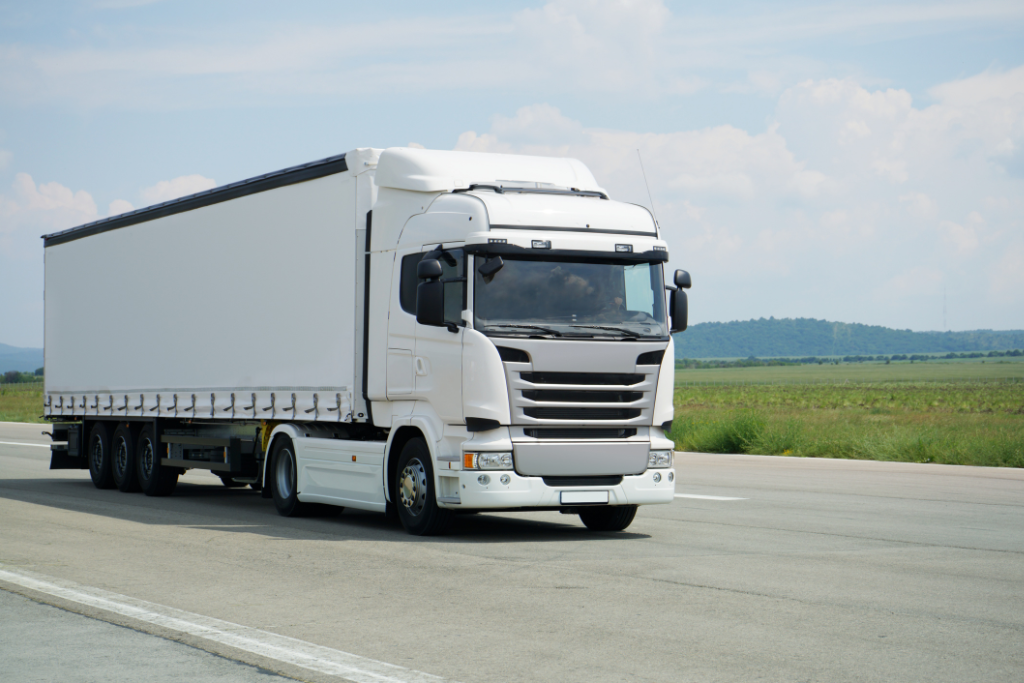 a white lorry on the road with a field behind and a mountain in the distance