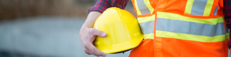 A man holding a yellow safety helmet in a hi-vis jacket