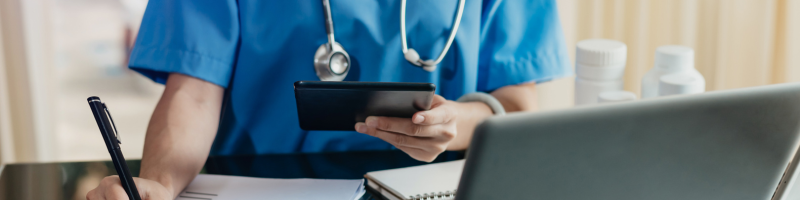 Nurse sitting at a desk in blue scrubs holding a device doing work